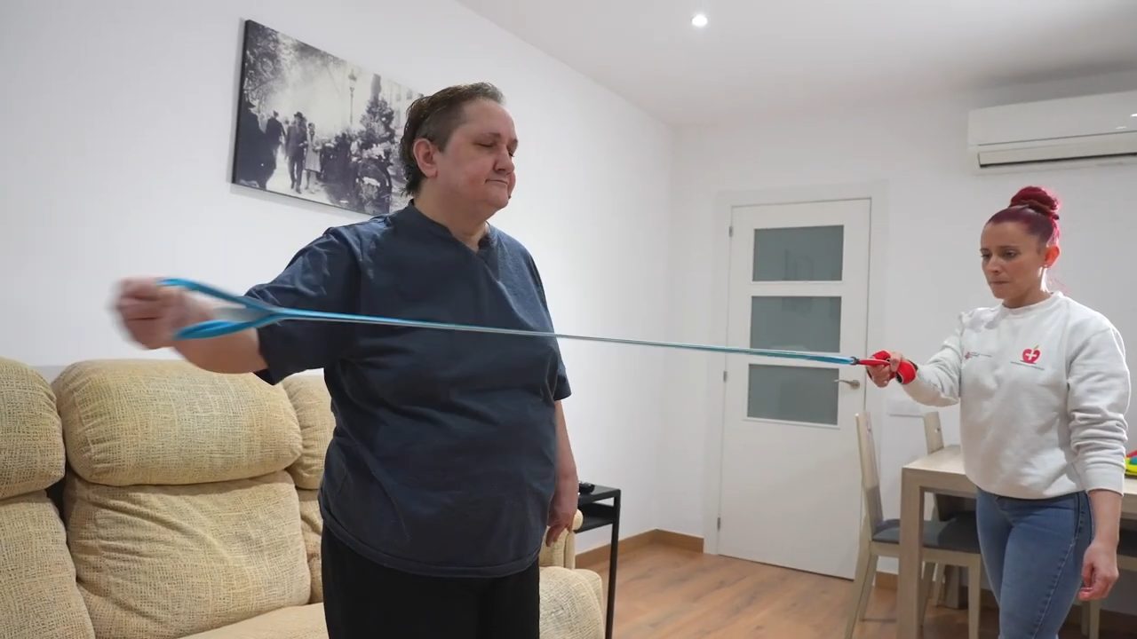 Fisioterapeuta guía un ejercicio de resistencia durante una sesión de rehabilitación neurológica en un domicilio